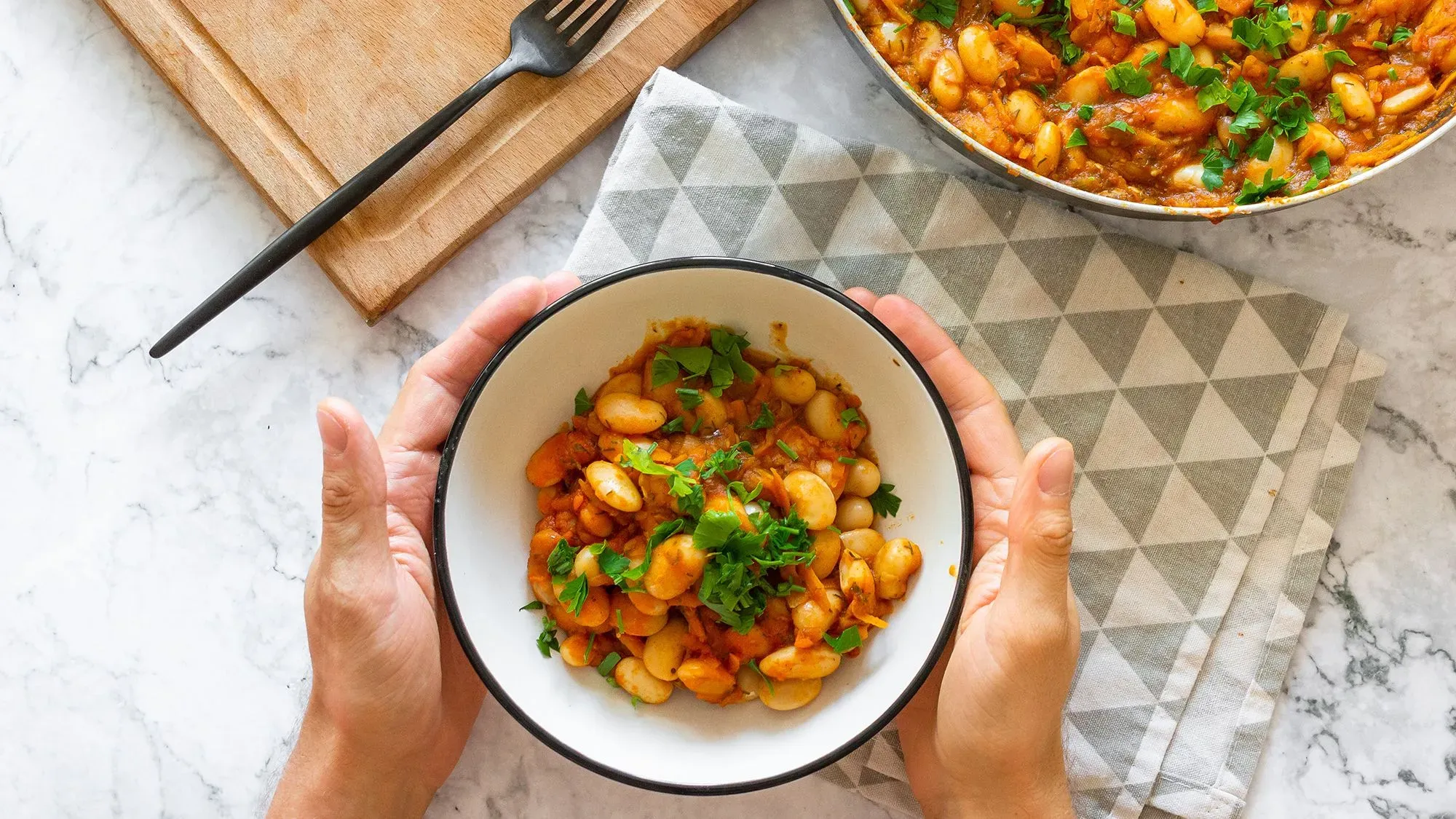 وعاء من الفاصولياء البيضاء مع صلصة الطماطم، مزين بالكزبرة، يُقدّم على مفرش مائل، مع شوكة خشبية بجانبه، يعكس أهمية البروتين في التغذية.