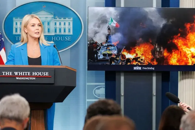 مستشارة البيت الأبيض تتحدث خلال مؤتمر صحفي، خلفها صورة لاحتجاجات عنيفة مع شعارات معادية.