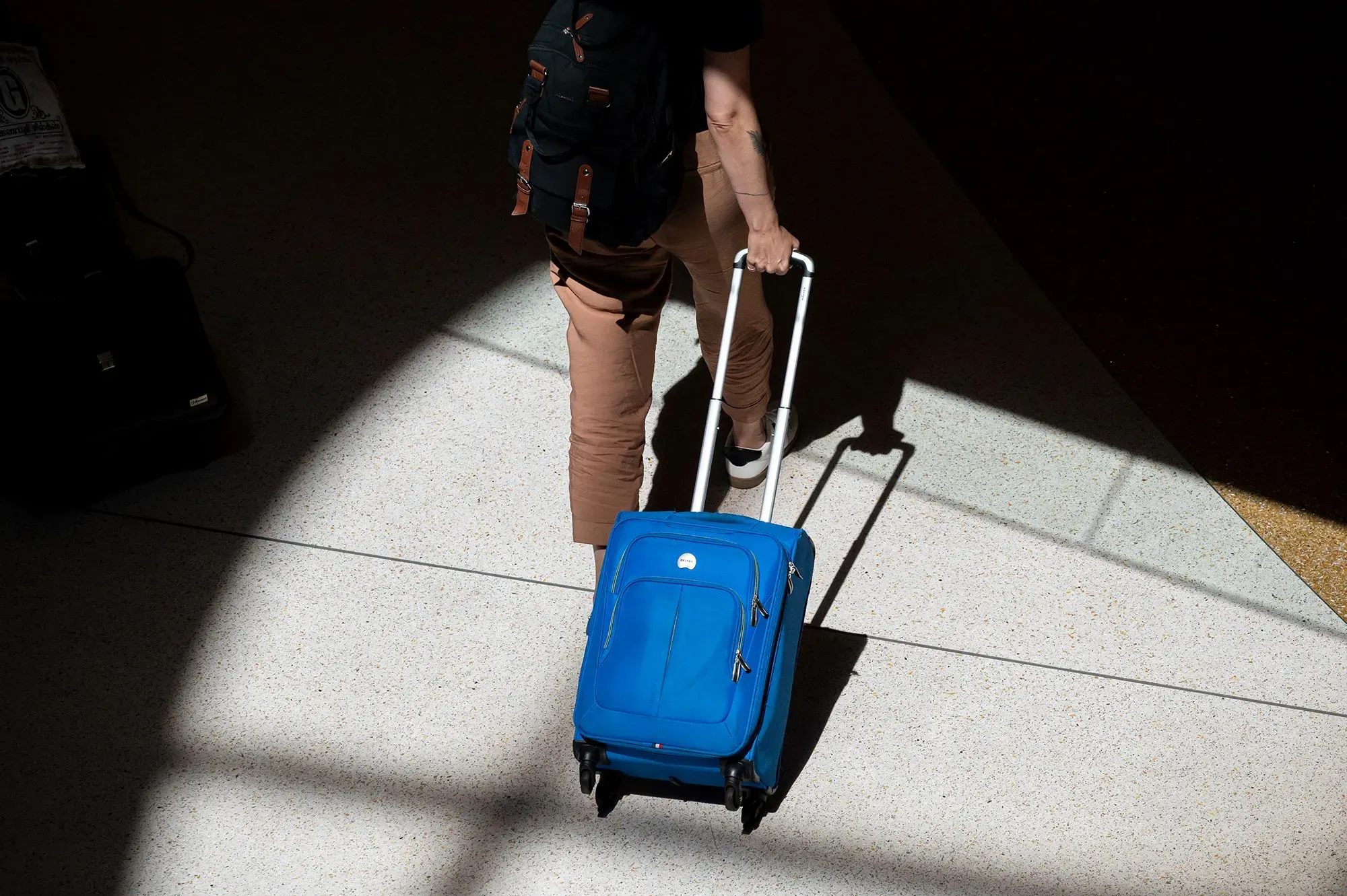 شخص يسير في مطار مع حقيبة سفر زرقاء، مما يعكس استعداد الأمريكيين للسفر في عطلة نهاية الأسبوع الأخيرة من الصيف.