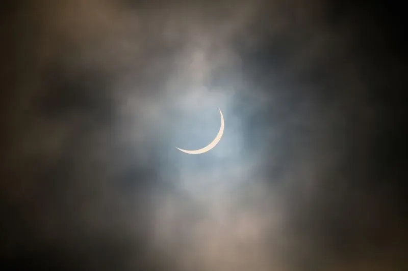 كسوف جزئي للشمس يظهر كقمر هلالي يمر أمام الشمس، محجوبًا جزئيًا، مع غيوم خفيفة في السماء.