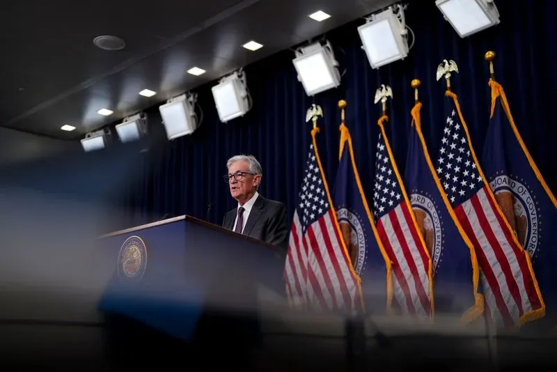 جيروم باول يتحدث في مؤتمر صحفي، خلفه أعلام الولايات المتحدة. يناقش الاستقلالية في قرارات الاحتياطي الفيدرالي وتأثيرها على الاقتصاد.