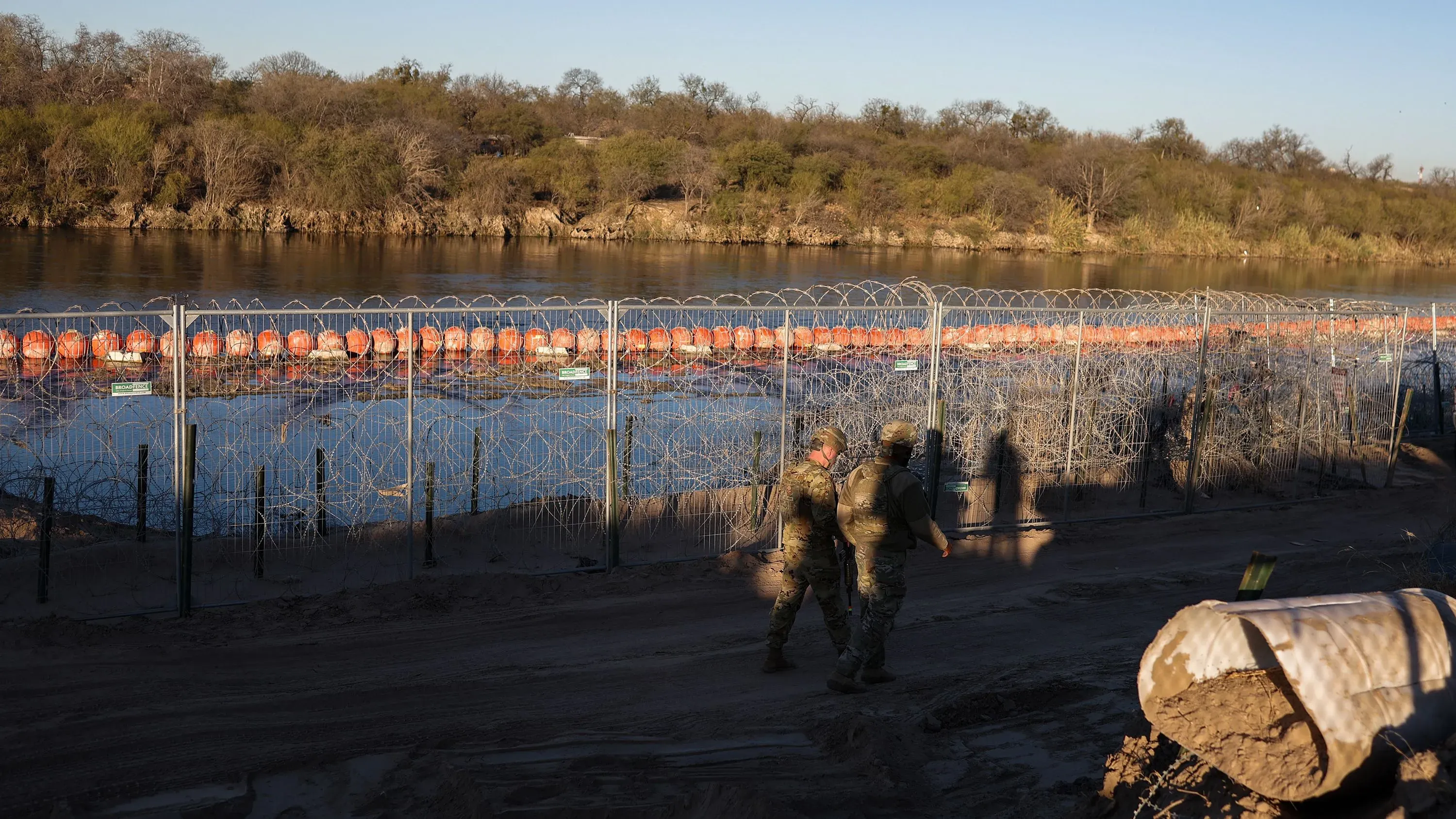 صورة لجنود يسيرون بجوار سياج شائك على الحدود الأمريكية المكسيكية، حيث تظهر العوائق المائية المستخدمة للحد من الهجرة غير القانونية.