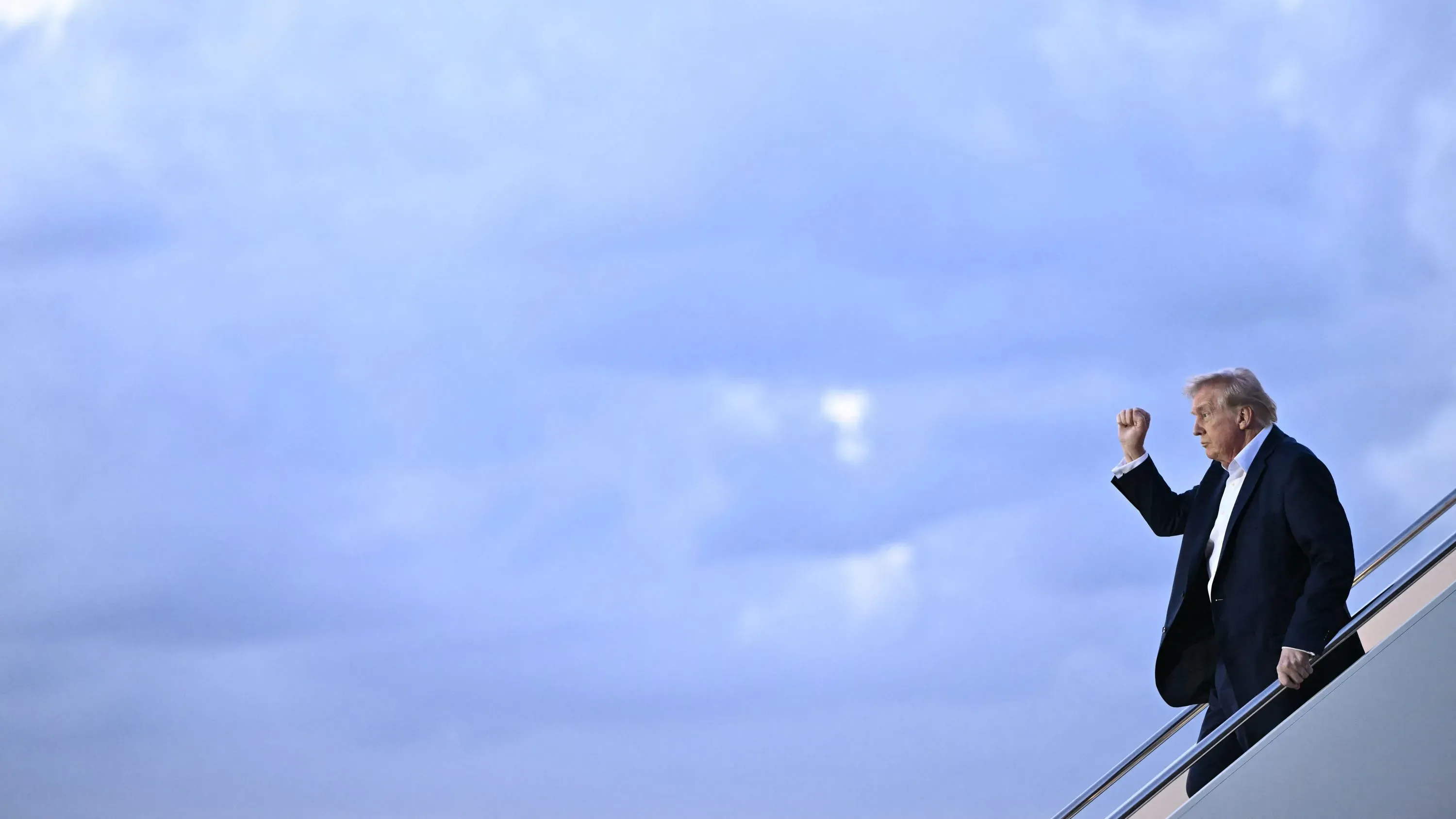 ترامب يلوح بيده من على الدرج في أجواء غائمة، معبراً عن طموحاته وسط الفوضى السياسية والاقتصادية التي تواجه إدارته.