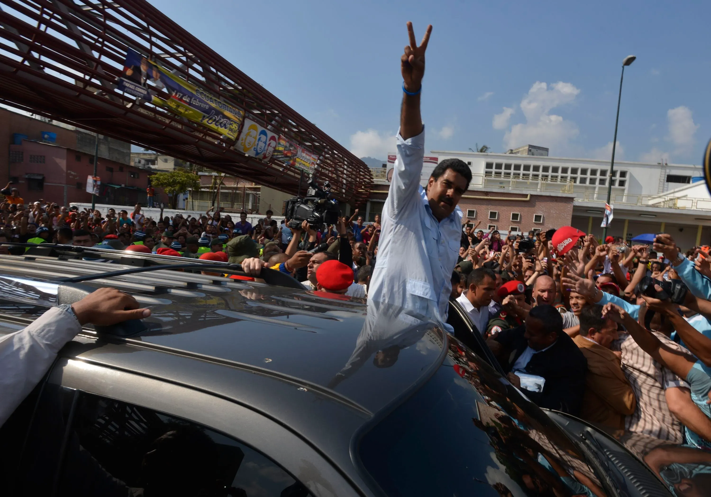 نيكولاس مادورو يرفع علامة النصر من فوق سيارة أثناء تجمع حاشد في فنزويلا، مع حشد من المؤيدين في الخلفية.