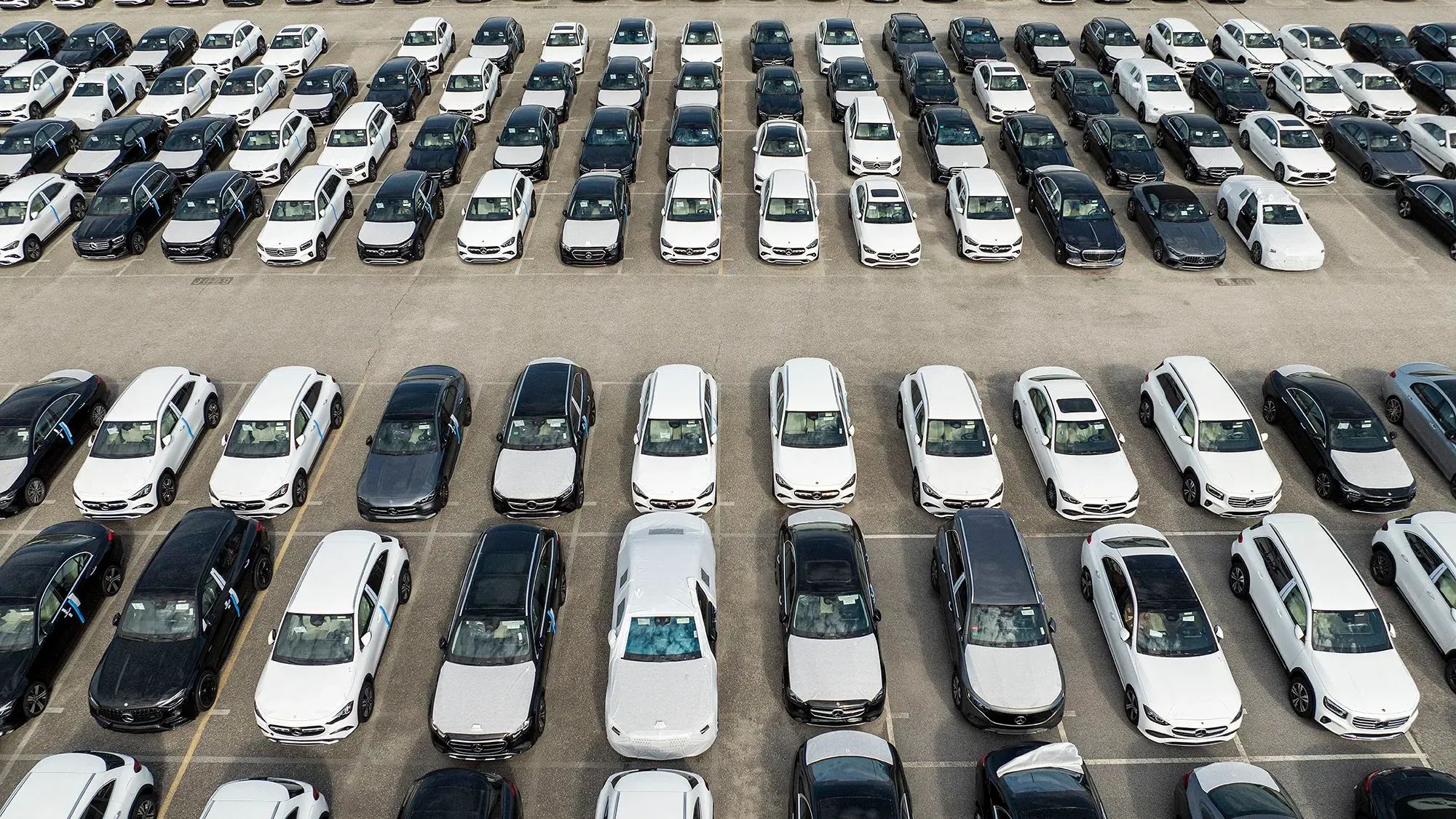 صف من السيارات الجديدة باللونين الأسود والأبيض في موقف سيارات واسع، يعكس تأثير الرسوم الجمركية على صناعة السيارات الأمريكية.