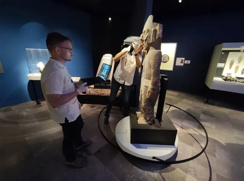 باحثون يستخدمون تقنية الأشعة السينية المحمولة لفحص قطعة أثرية من حجر السبج في متحف، وسط خلفية مظلمة.