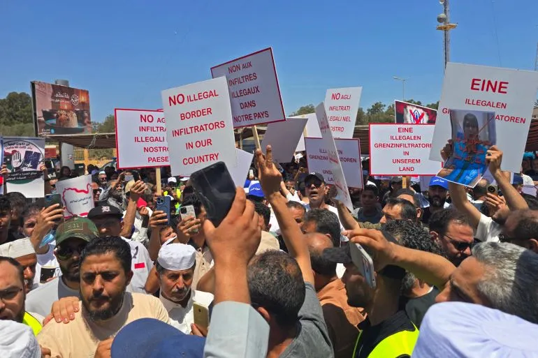 تجمع حشود من الليبيين أمام المفوضية السامية للأمم المتحدة للاجئين في طرابلس، حاملين لافتات تعبر عن رفضهم للمهاجرين غير الموثقين.