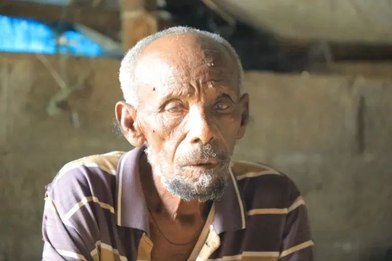 رجل مسن يجلس في مكان بسيط، يعكس ملامحه معاناة الجوع والنزوح في تيغراي، إثيوبيا، حيث يواجه تحديات إنسانية كبيرة.