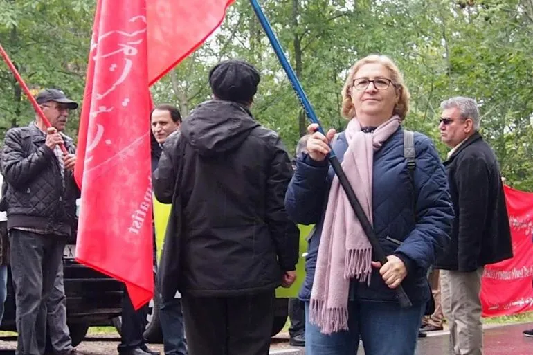 امرأة تحمل علمًا أحمر وسط مجموعة من المتظاهرين في السويد، تعبيرًا عن احتجاجات ضد قوانين الهجرة الصارمة.