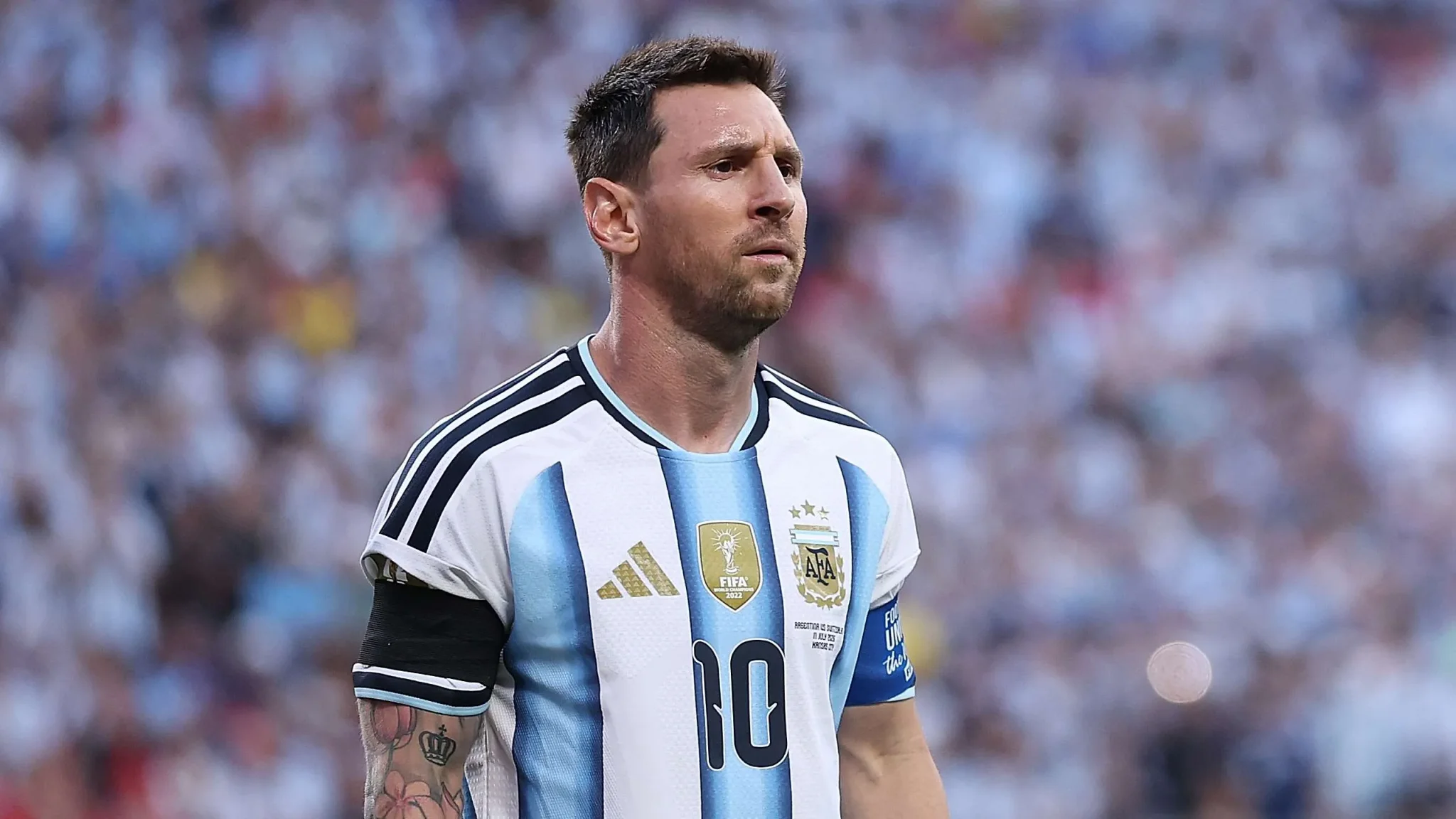 ليونيل ميسي يرتدي زي منتخب الأرجنتين لكرة القدم، يظهر بتعبير وجه جاد خلال مباراة، مع شارة القيادة على ذراعه، في لحظة تعكس تحديات مستقبله الكروي بعد وفاة والده.