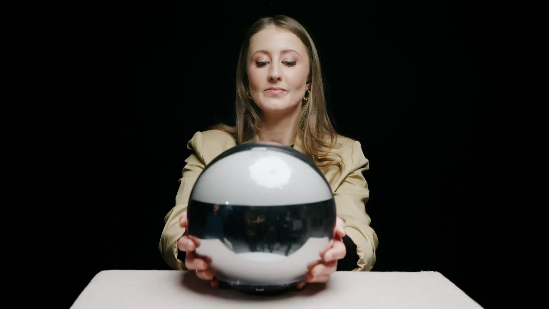 امرأة تحمل كرة فضية تعكس الضوء، بينما تجلس أمام خلفية داكنة، تشير إلى تقنية التحقق من الهوية باستخدام Orb.