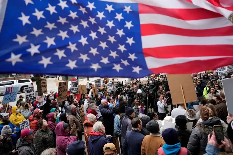 تجمع حاشد أمام قاعة المحكمة في بوسطن، حيث يرفع المتظاهرون لافتات احتجاجية بينما ترفرف علم الولايات المتحدة في الخلفية.
