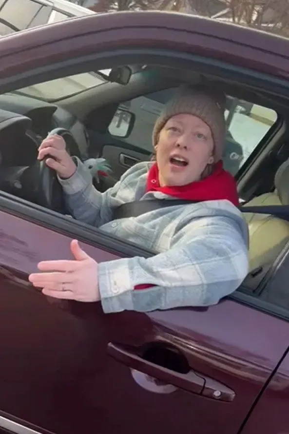 امرأة تجلس في سيارة، تتحدث وتبدو متفاجئة أو غاضبة، مع التركيز على تفاعلها أثناء عملية تتعلق بالهجرة.