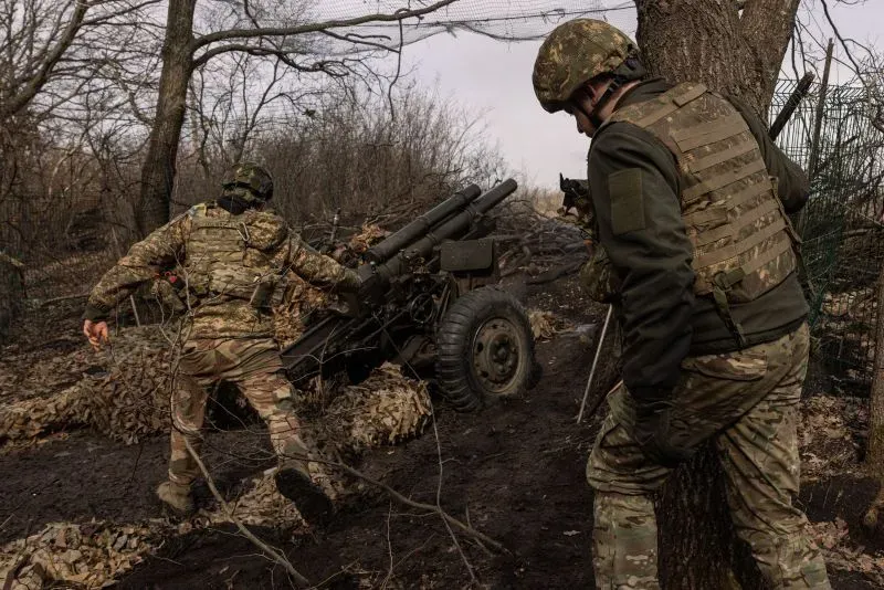 جنود يرتدون زيًا عسكريًا، يعملون على مدفع ميداني في منطقة غابية، مما يعكس التوترات العسكرية الحالية وتأثيرها على السياسة العالمية.