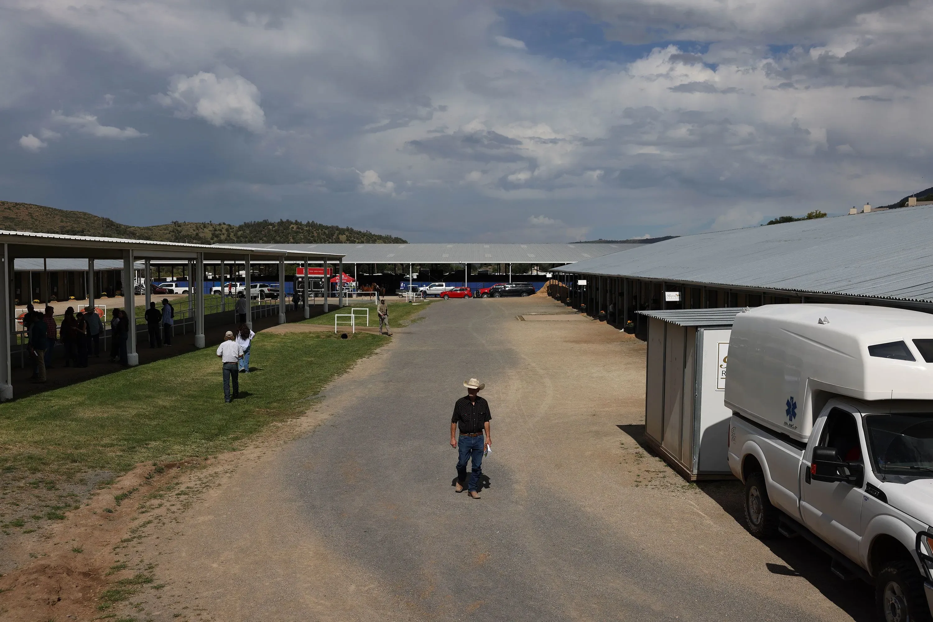 صورة لشارع في روي دوسو، نيو مكسيكو، حيث يتجمع الناس تحت مظلات، في ظل سماء غائمة، استعداداً لمزاد بيع الخيول.