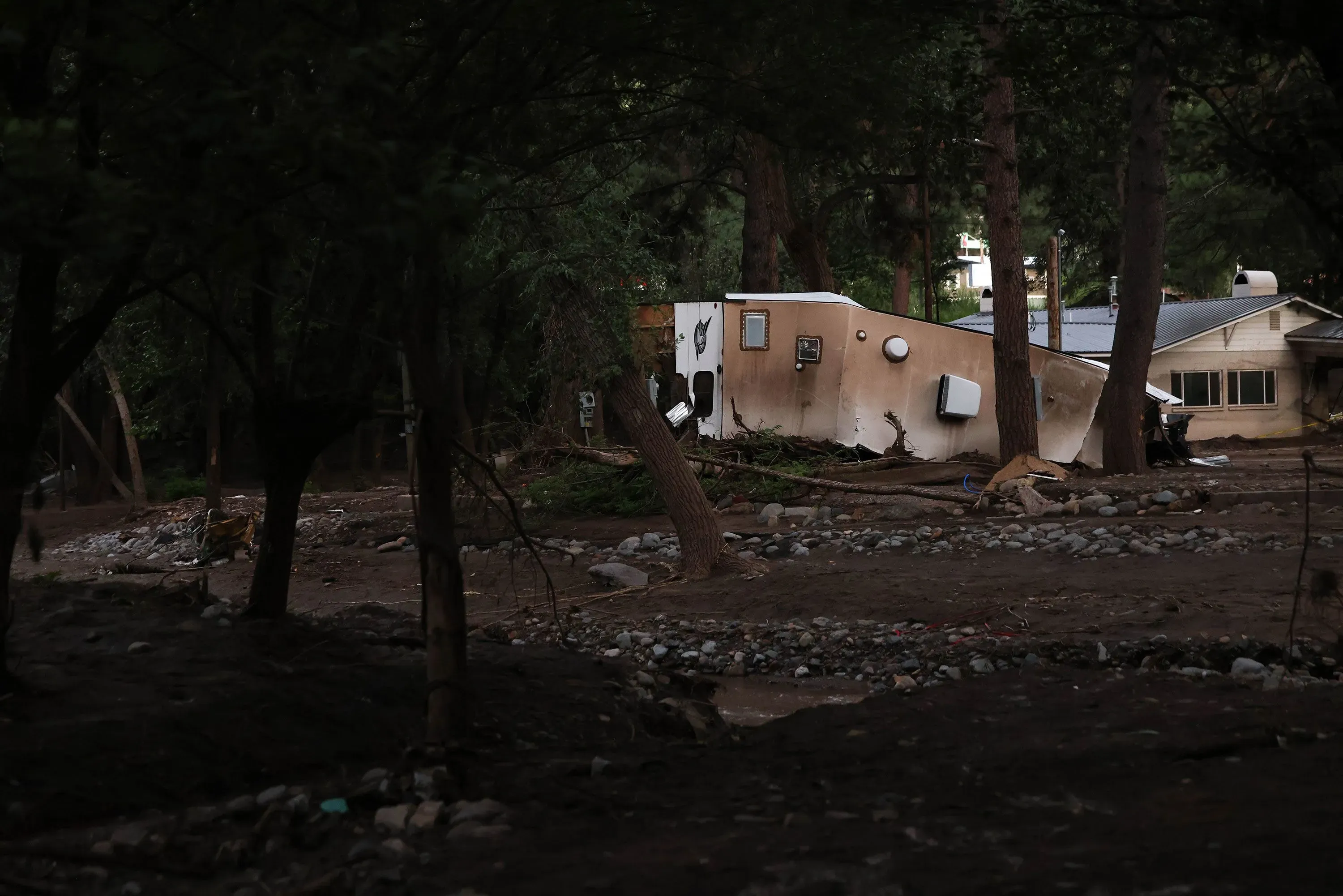 منزل مائل وسط غابة، محاط بأشجار، بعد الفيضانات المدمرة في رويدوسو، نيو مكسيكو، مع بقايا الطين والحطام حوله.