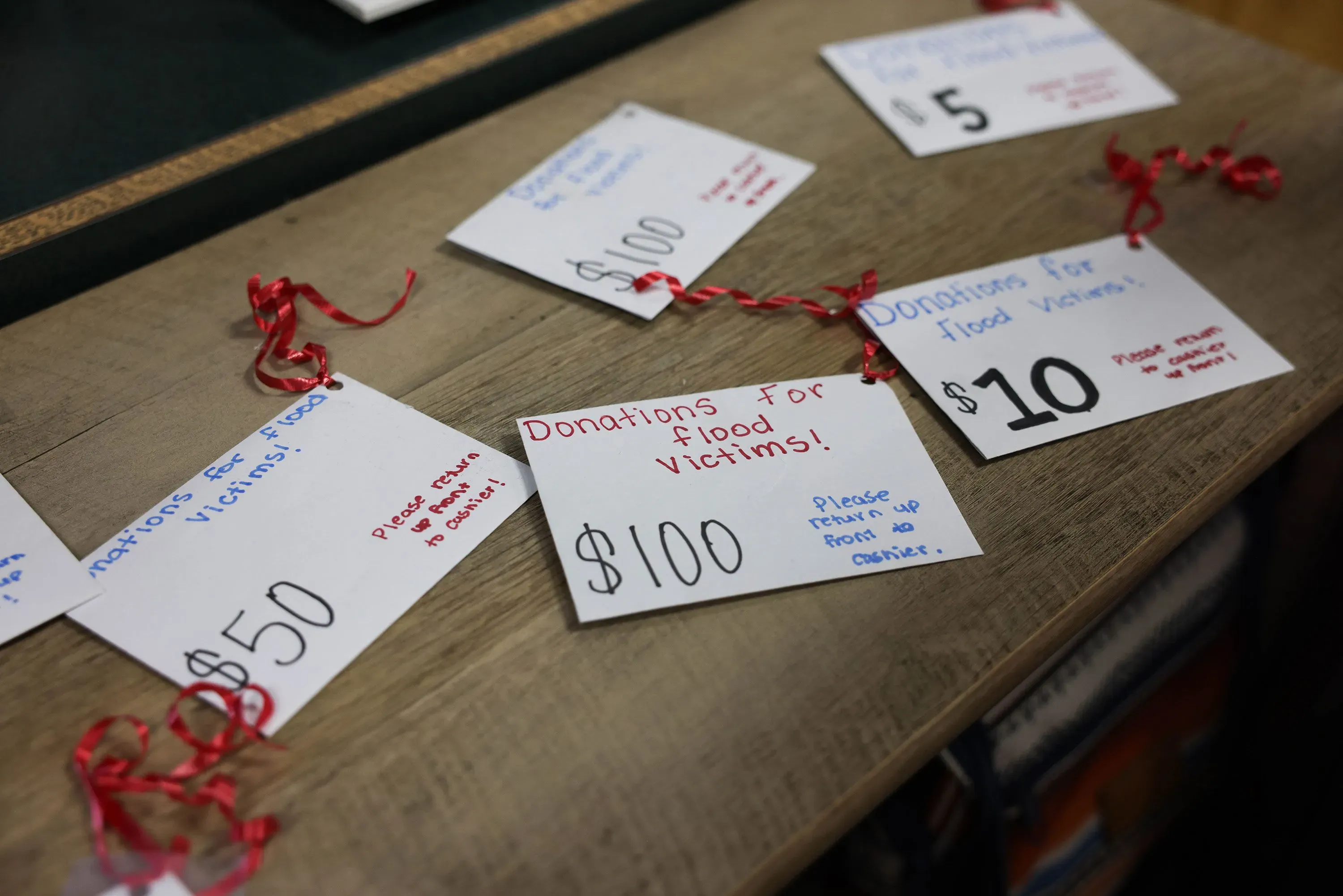 بطاقات تبرع مكتوبة بخط اليد لأغراض ضحايا الفيضانات، تتضمن مبالغ مختلفة مثل 5 و10 و50 و100 دولار، موضوعة على طاولة.