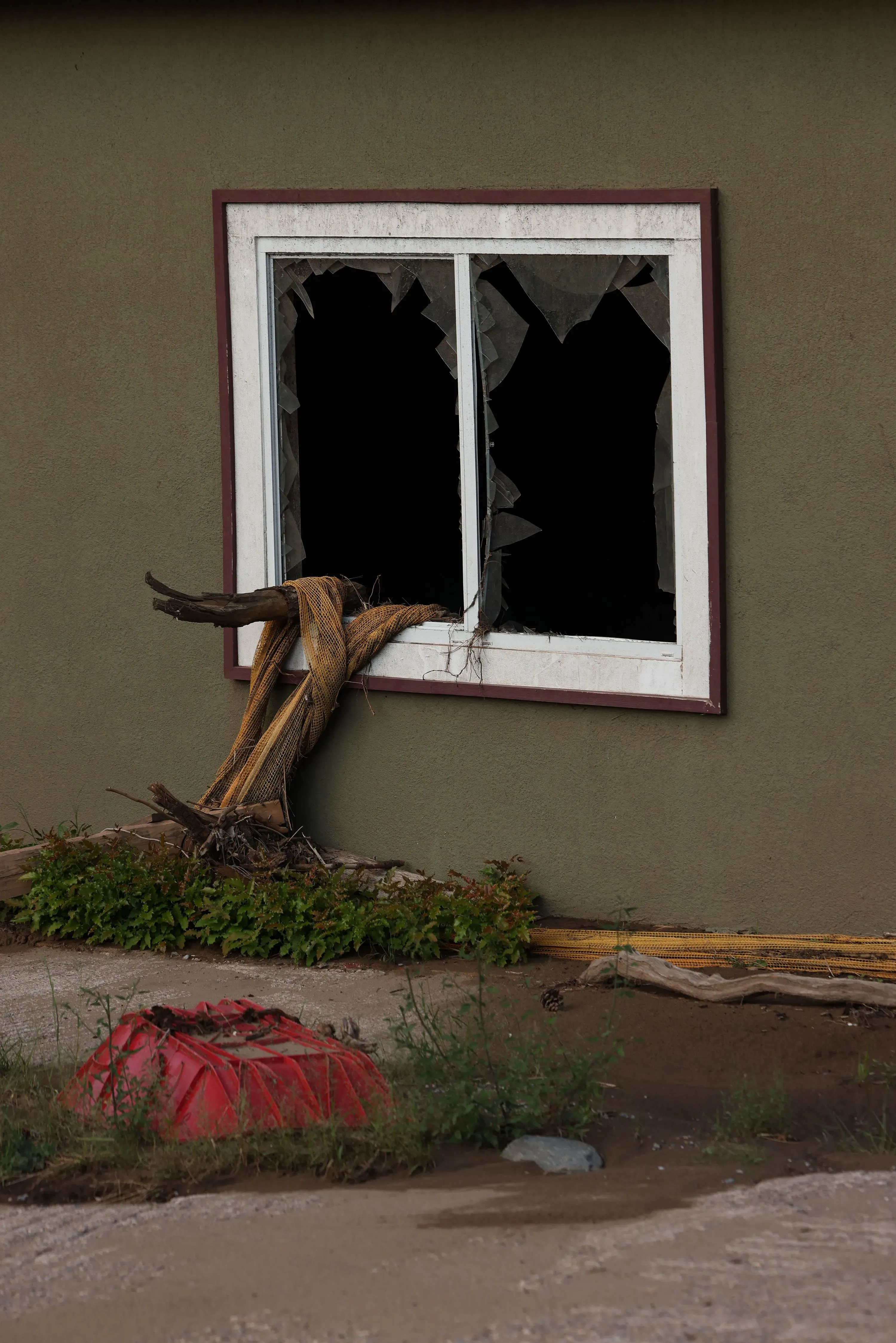 شباك مكسور في منزل متضرر بفعل الفيضانات، مع حطام وأغراض ملقاة حوله، تعكس آثار الكارثة في رويدوسو.