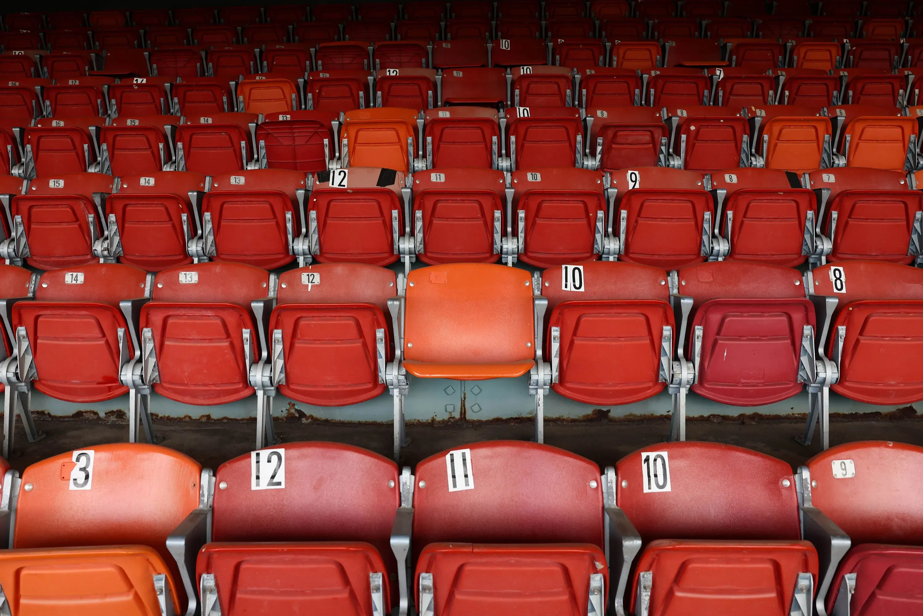 صفوف من المقاعد الحمراء في مدرج فارغ، مع مقعد برتقالي يتوسطها، تعكس غياب الحشود في مضمار سباق رويدوسو المتضرر.