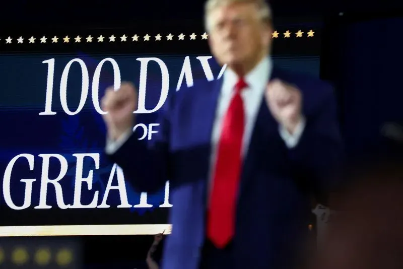 دونالد ترامب يتحدث في حدث عام، مع لافتة خلفية تحمل عبارة "100 يوم من العظمة"، مما يعكس أوجه التشابه بينه وبين الثورة الثقافية في الصين.