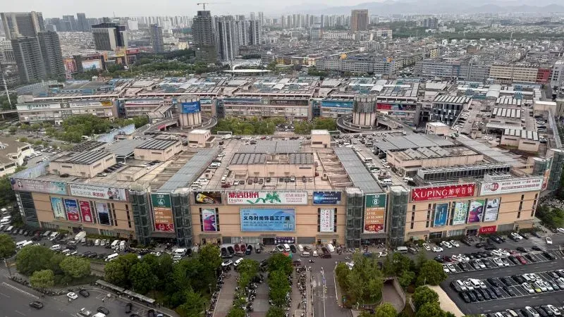 منظر جوي لمجمع سوق ييوو في الصين، المعروف بتصدير زينة عيد الميلاد، مع وجود سيارات وحدائق حول المباني التجارية.