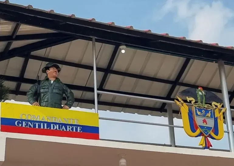 تمثال لجندي يرتدي زيًا عسكريًا، يقف تحت لافتة تحمل اسم "الكوماندانتي جينتيلي دوارتي"، مع شعار كولومبيا في الخلفية.