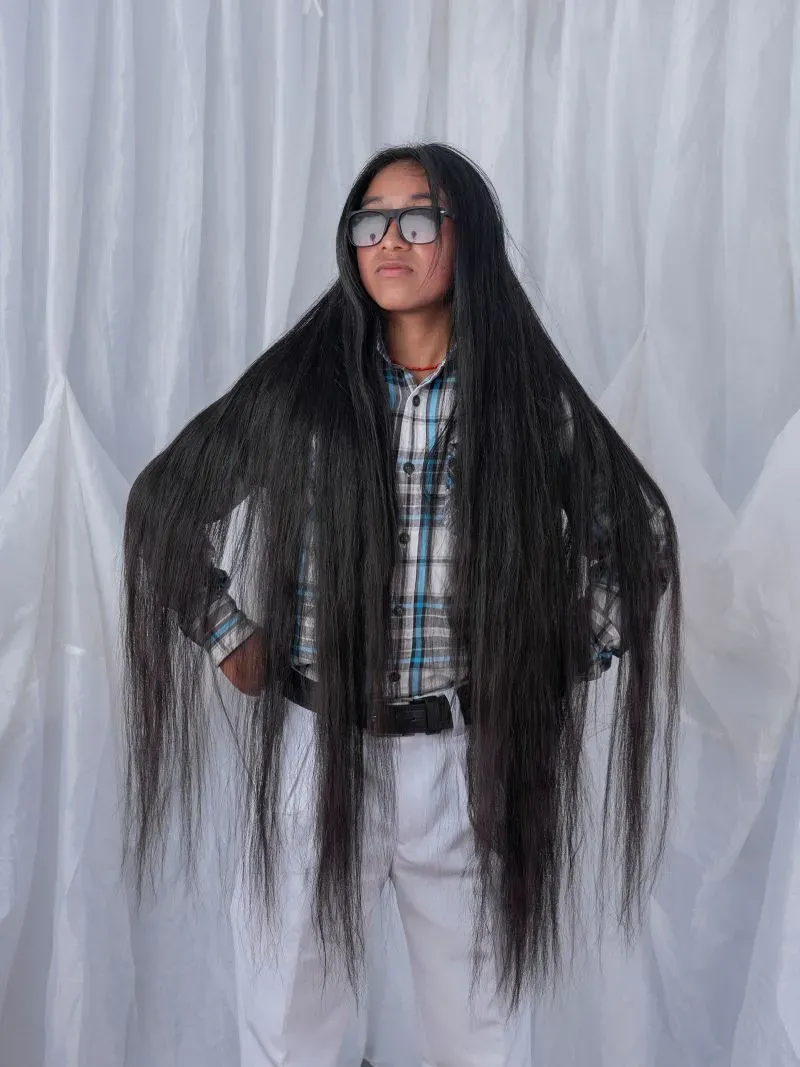 شخص يرتدي نظارات ويقف بفخر مع شعره الطويل الذي يتدلى من الجانبين، يعكس ثقافة الهوية والتقاليد في مجتمعات كيشوا.