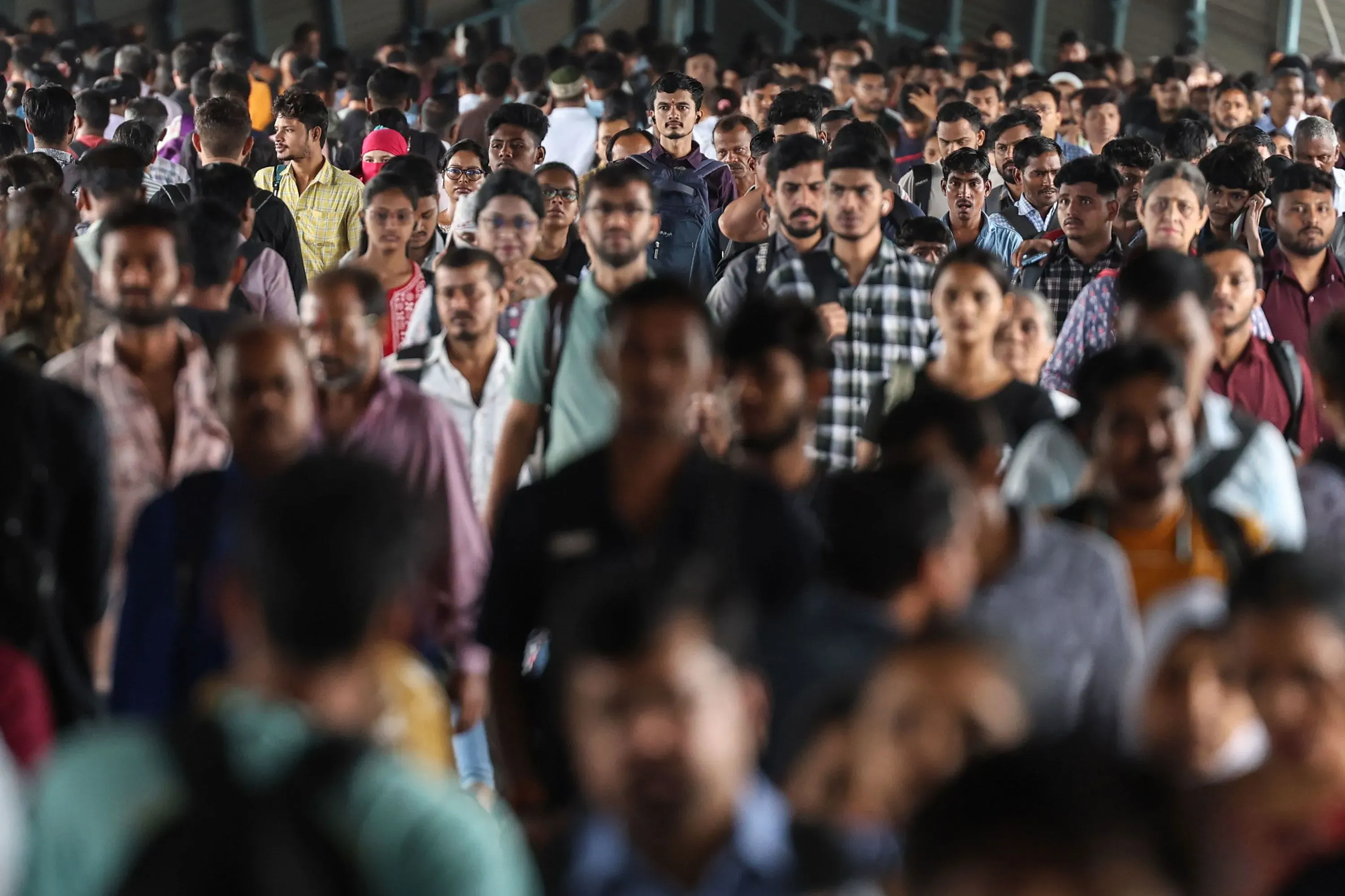حشود من العمال في الهند يتجمعون في محطة، يعكسون الضغط المتزايد على عمال التوصيل بسبب متطلبات العمل الصعبة.
