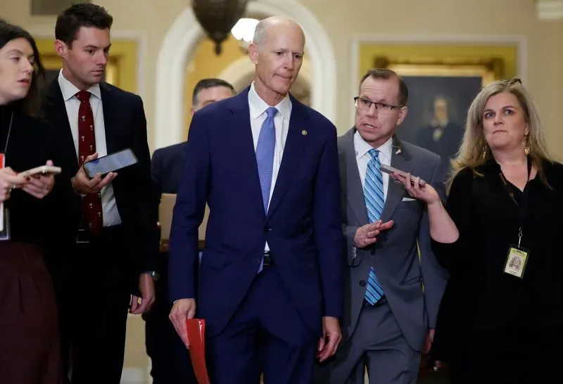 مجموعة من الأشخاص، بينهم السيناتور ريك سكوت، يتحدثون في ممر الكونغرس، مع تركيز على النقاش حول سياسة الحزب الجمهوري وأجندة ترامب.