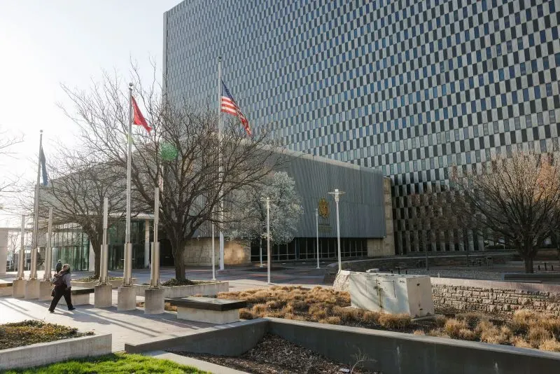 واجهة مبنى حكومي في مدينة كانساس سيتي، مع أعلام مرفوعة وأشجار، تعكس تأثير تسريح العمال الفيدراليين على الاقتصاد المحلي.