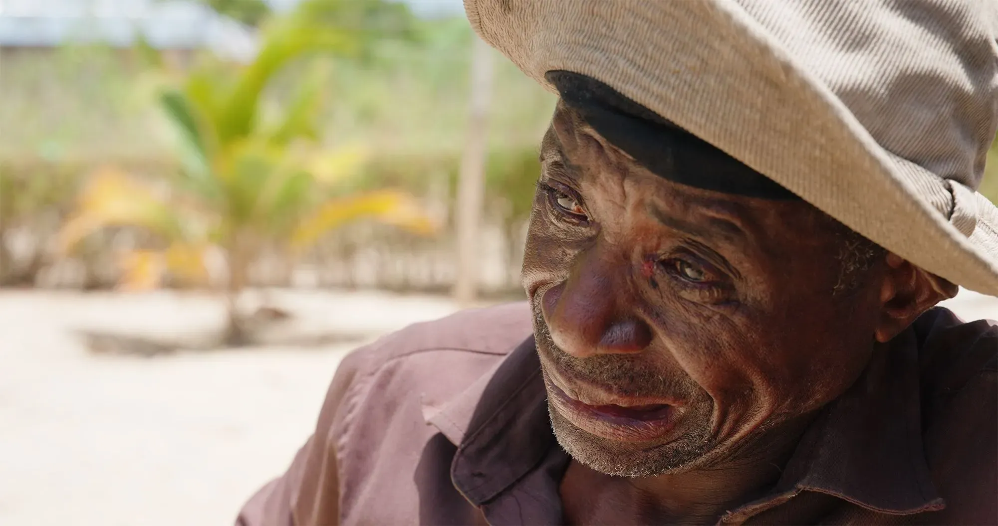 وجه رجل مسن يرتدي قبعة، يظهر عليه الحزن والتعب، في خلفية خضراء. تعكس ملامحه تأثير الصراع والفقر في موزمبيق.