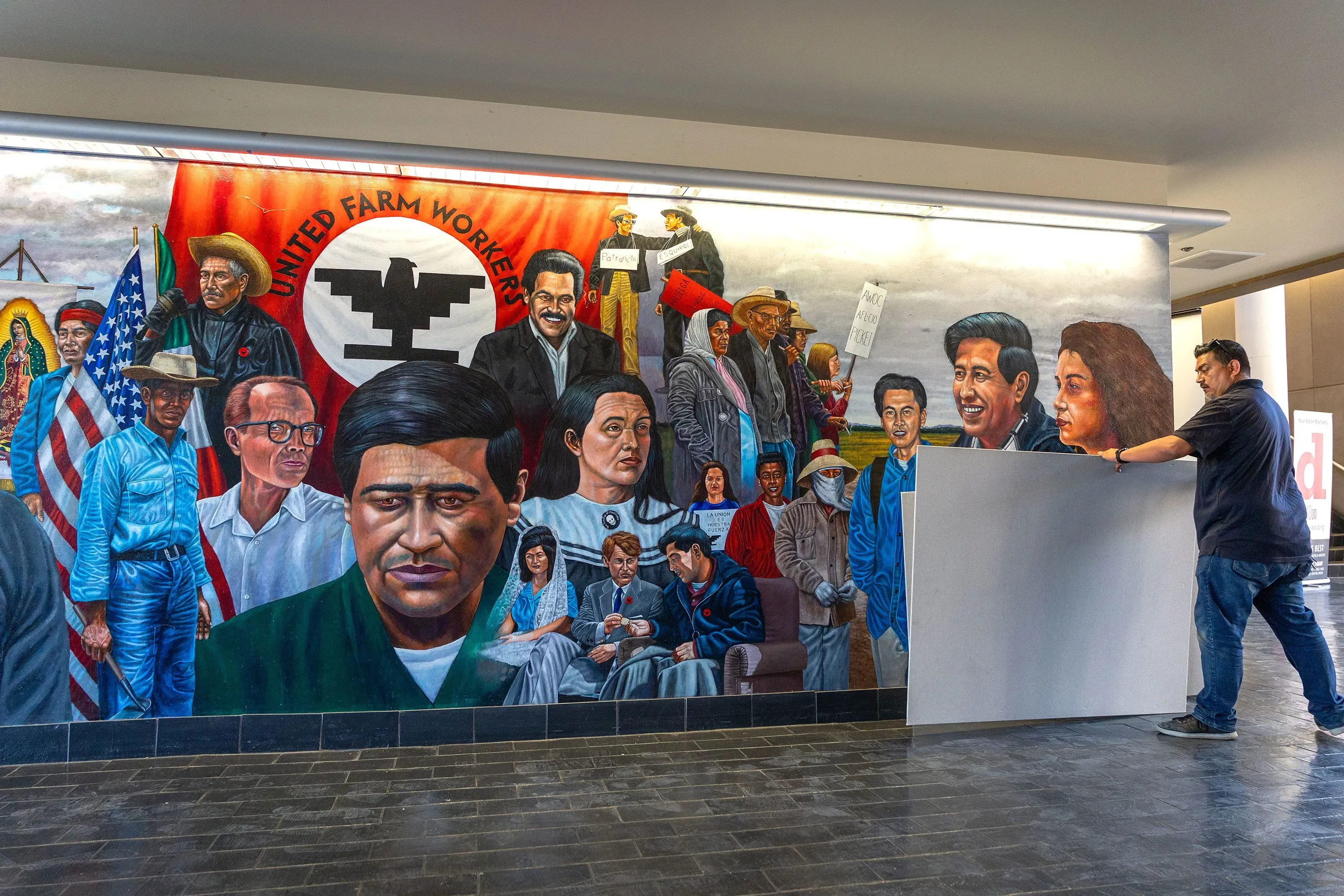 رجل يقوم بتغطية جدارية تصور سيزار تشافيز وعمال المزارع، في سياق إعادة تقييم إرثه بعد اتهامات جديدة.