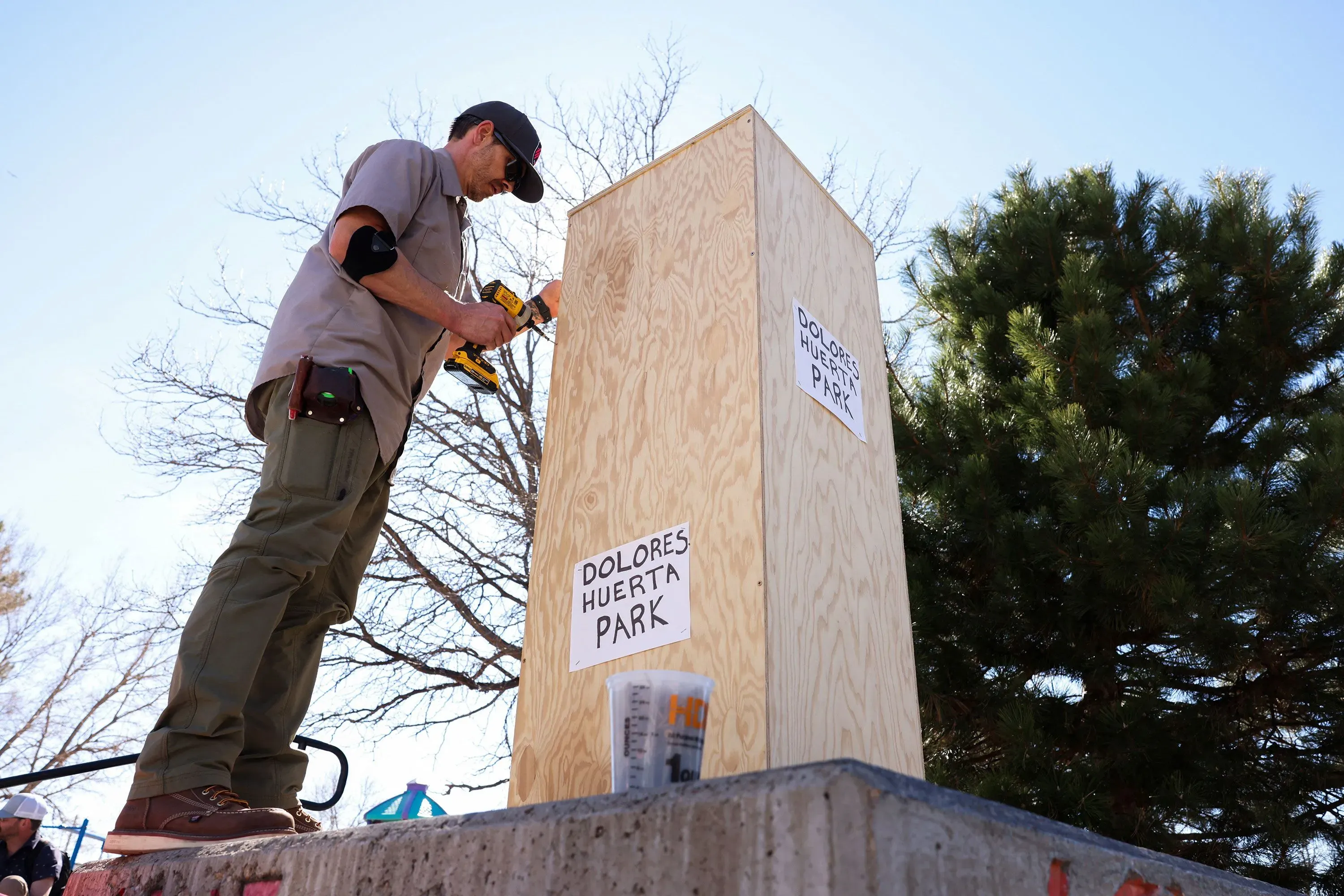 عامل يقوم بتغطية قاعدة تمثال سيزار تشافيز في حديقة دولوريس هويرتا، بعد مزاعم الاعتداء الجنسي، مع لافتة تحمل اسم الحديقة.