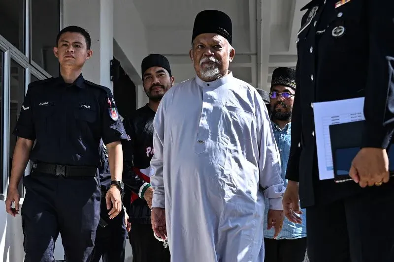 رجل مسن يرتدي ملابس تقليدية ويبدو أنه يتحدث مع رجال الشرطة أثناء مغادرته مبنى، في سياق مداهمات لدار رعاية في ماليزيا.