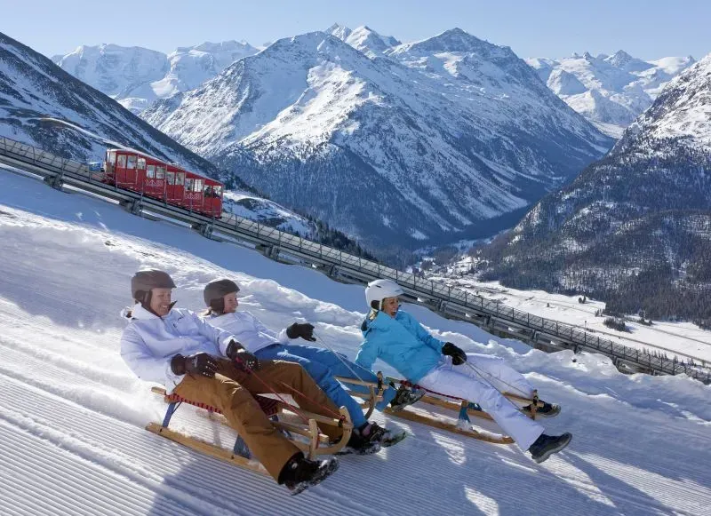 مجموعة من الأشخاص يتزلجون على زلاجات في جبال الألب السويسرية، مع مناظر طبيعية ثلجية خلابة وخطوط تلفريك في الخلفية.