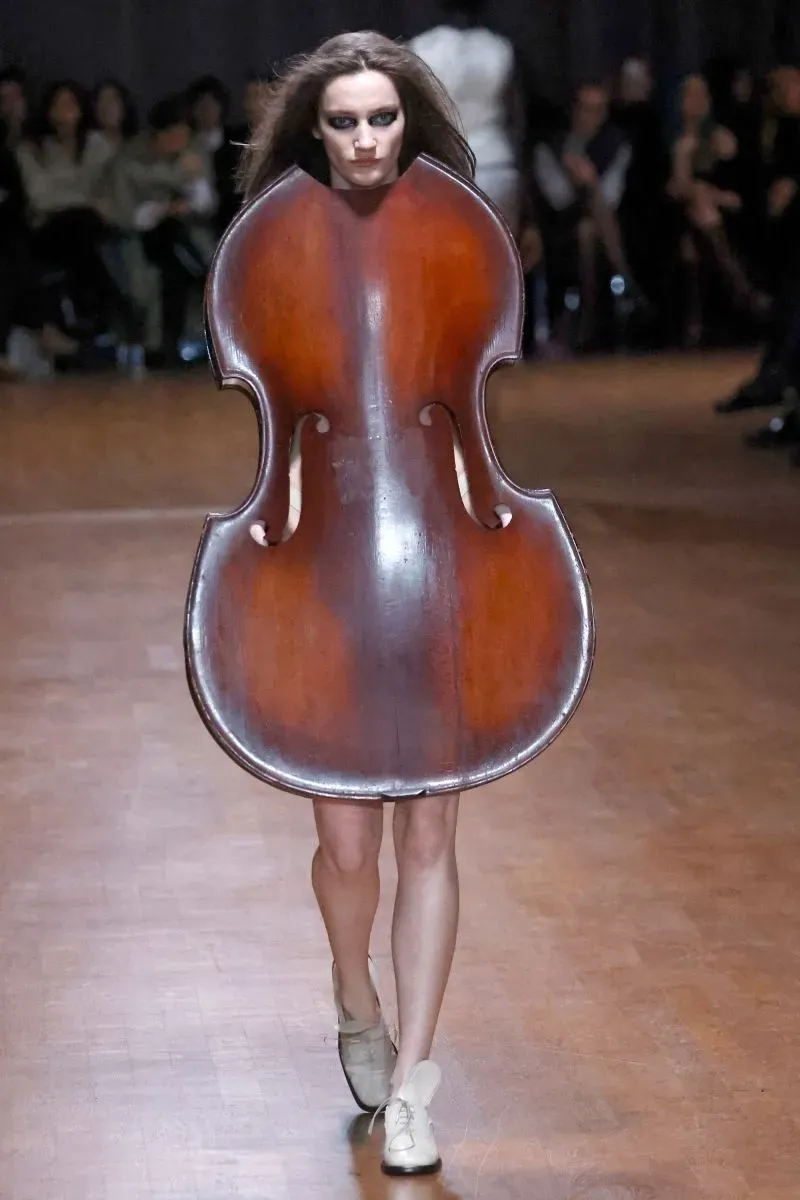 عارضة أزياء ترتدي تصميمًا مبتكرًا يشبه آلة التشيلو، مما يعكس أسلوب المصممة إلين هوداكوفا لارسون في تحويل المواد غير التقليدية إلى أزياء راقية.