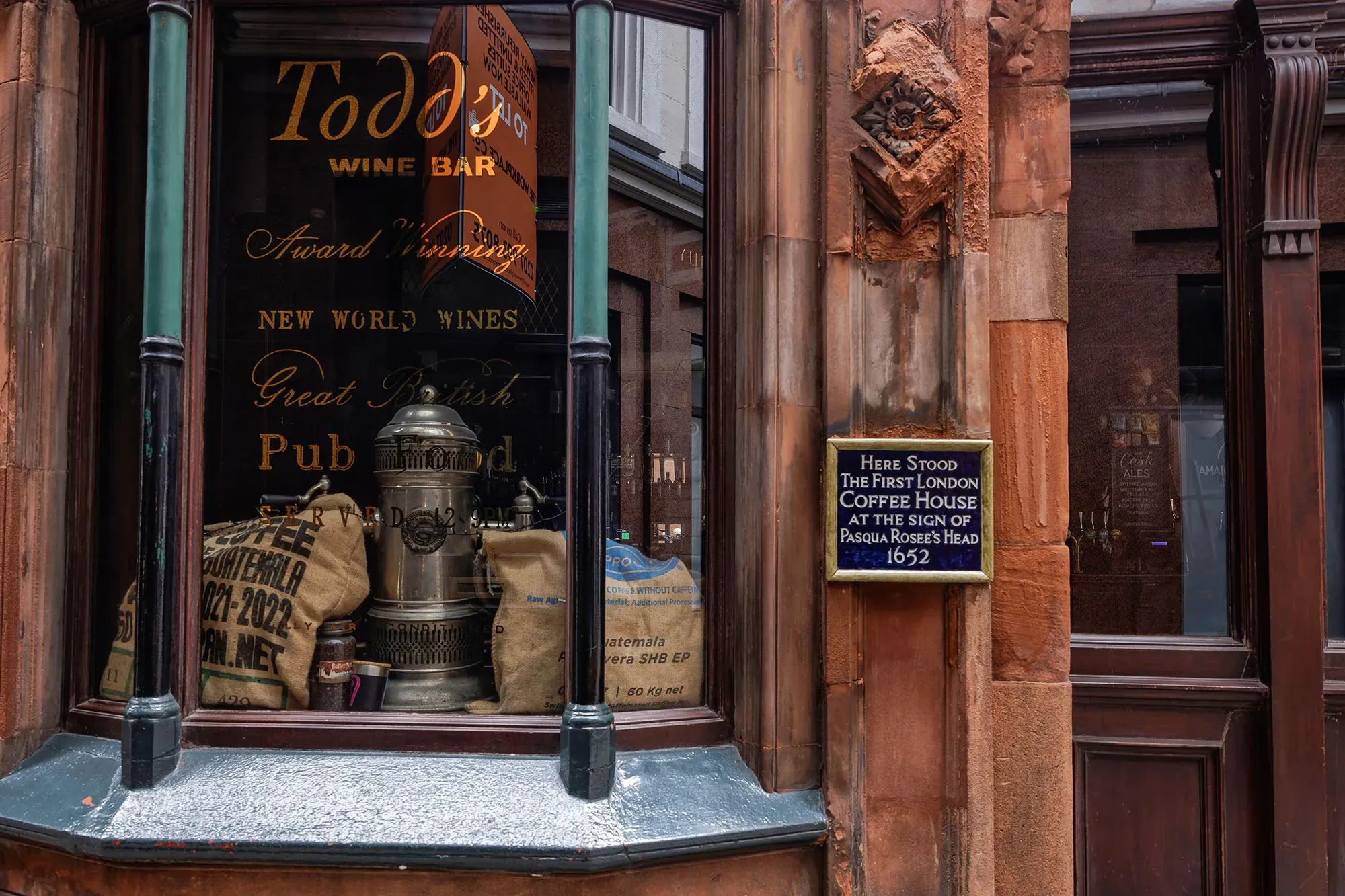 واجهة مقهى تاريخي في لندن، تعرض لافتة تشير إلى أول مقهى في المدينة، مع تفاصيل عن القهوة والتقاليد الثقافية.