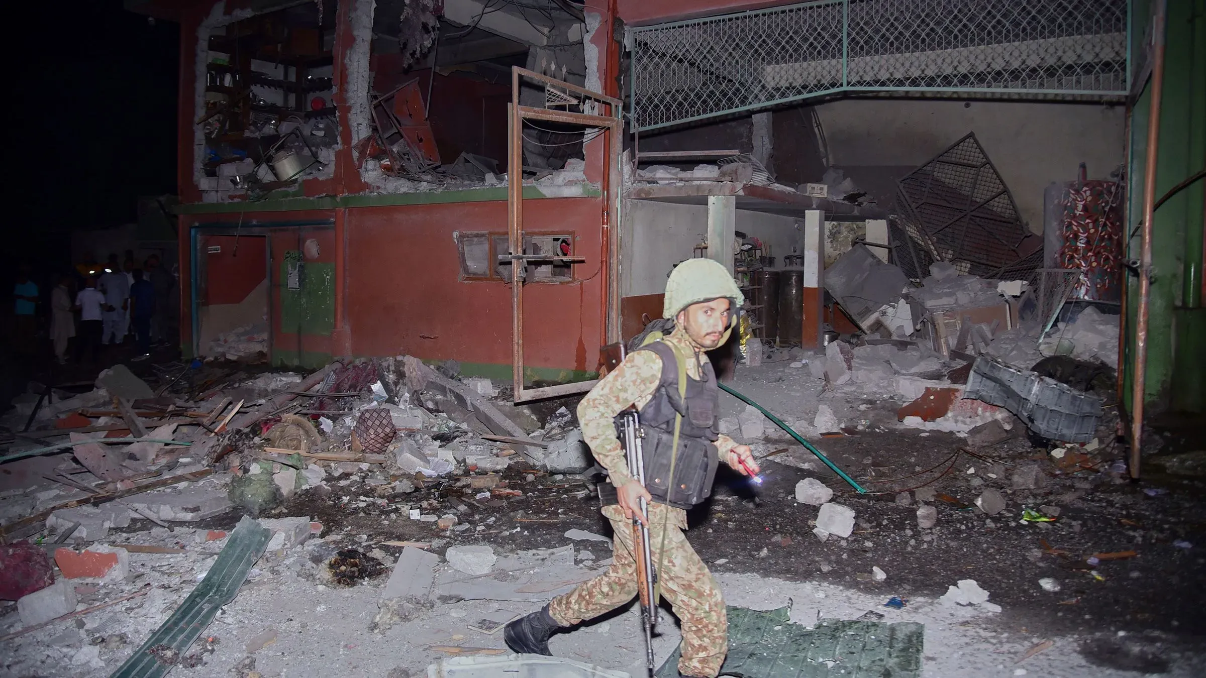 جندي باكستاني يسير بين حطام مبنى مدمر بعد غارات جوية هندية، مع وجود أشخاص في الخلفية، مما يعكس تصعيد التوترات بين الهند وباكستان.