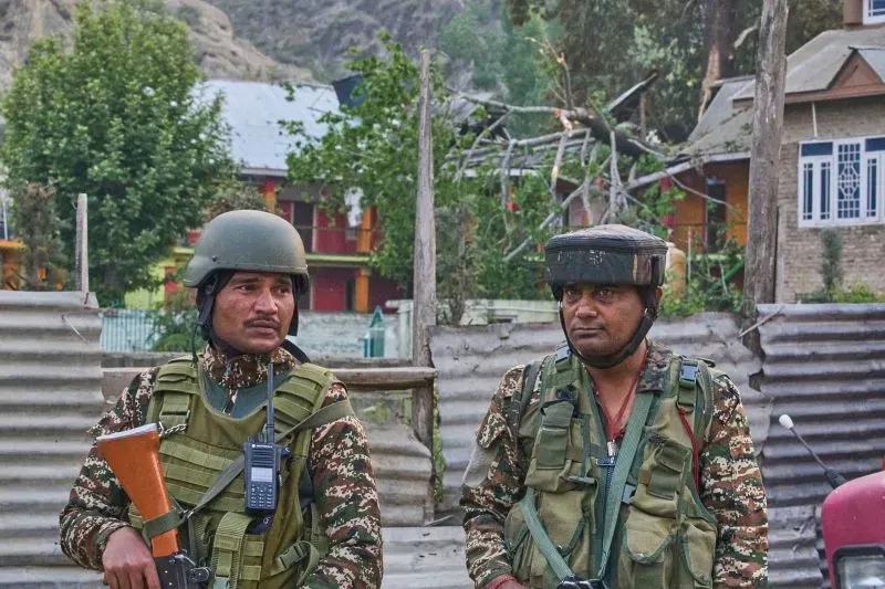 جنود هنديون يرتدون زياً عسكرياً خلال تصاعد التوترات بين الهند وباكستان، في خلفية تظهر منازل محلية وأشجار متضررة.