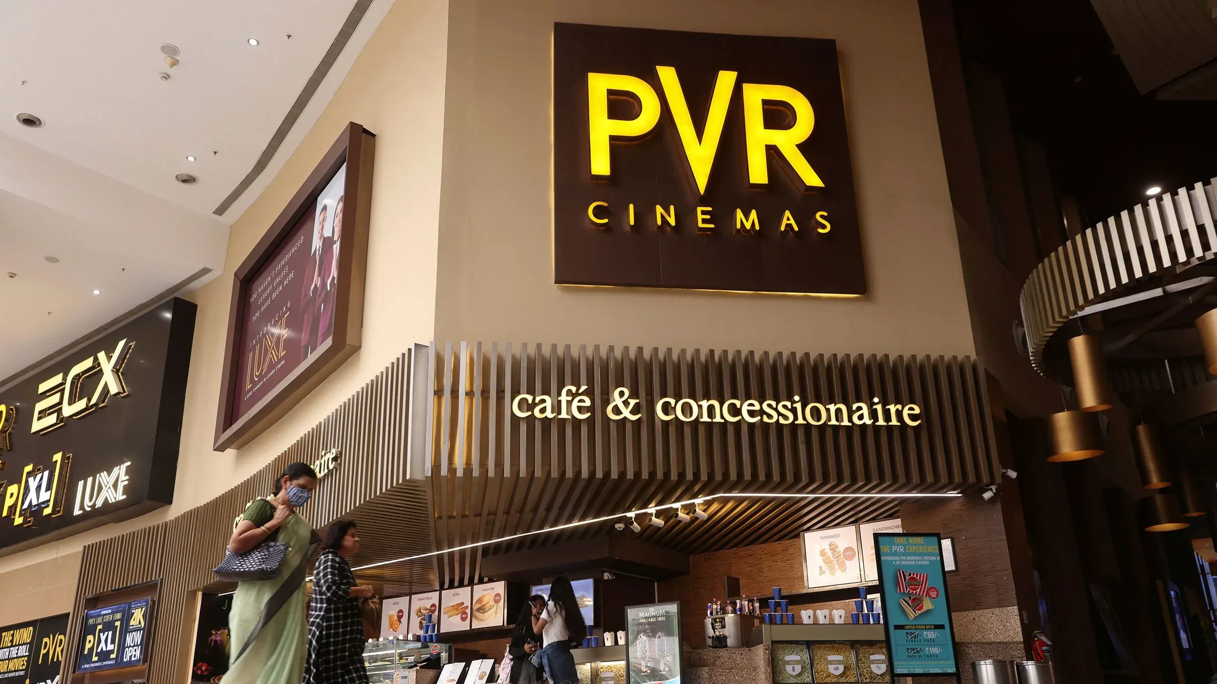 مدخل سينما PVR مع لافتة مضيئة، حيث يتواجد زوار يتجهون نحو كافيتيريا وصالة العرض، في سياق قضية قانونية حول الإعلانات.