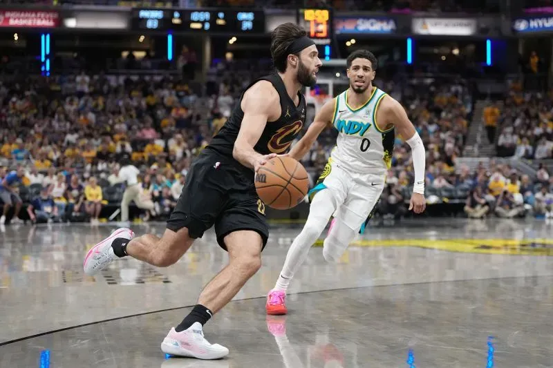 لاعب من فريق كليفلاند كافالييرز يحمل الكرة بينما يتبعه لاعب من فريق إنديانا بيسرز خلال مباراة البلاي أوف، مع جمهور في الخلفية.