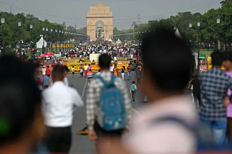 مشهد حيوي لشارع مزدحم في الهند، حيث يتجمع الناس أمام نصب الهند، مما يعكس تأثير النظام الطبقي على الحياة اليومية.