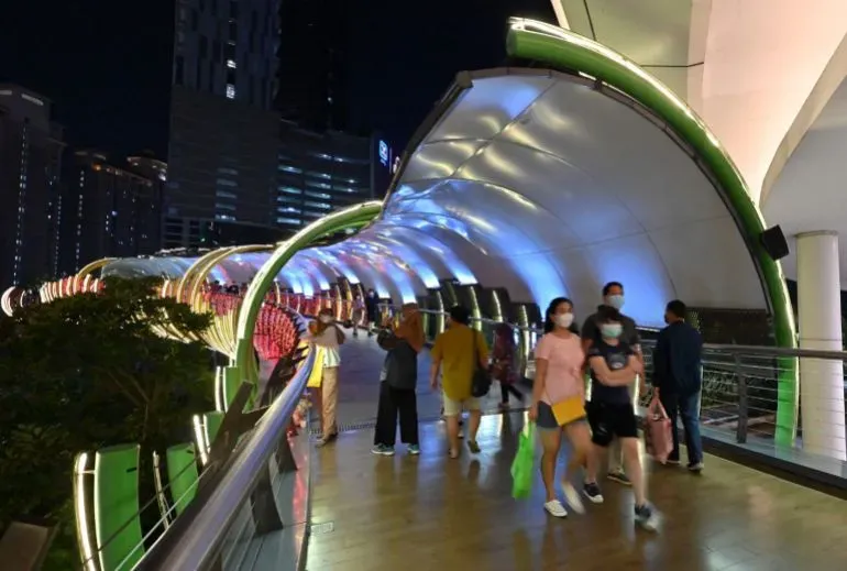 مشاة يتجولون في ممر مضاء بألوان زاهية في مركز تسوق بإندونيسيا، يعكس تراجع القوة الشرائية وسلوكيات التسوق الجديدة.