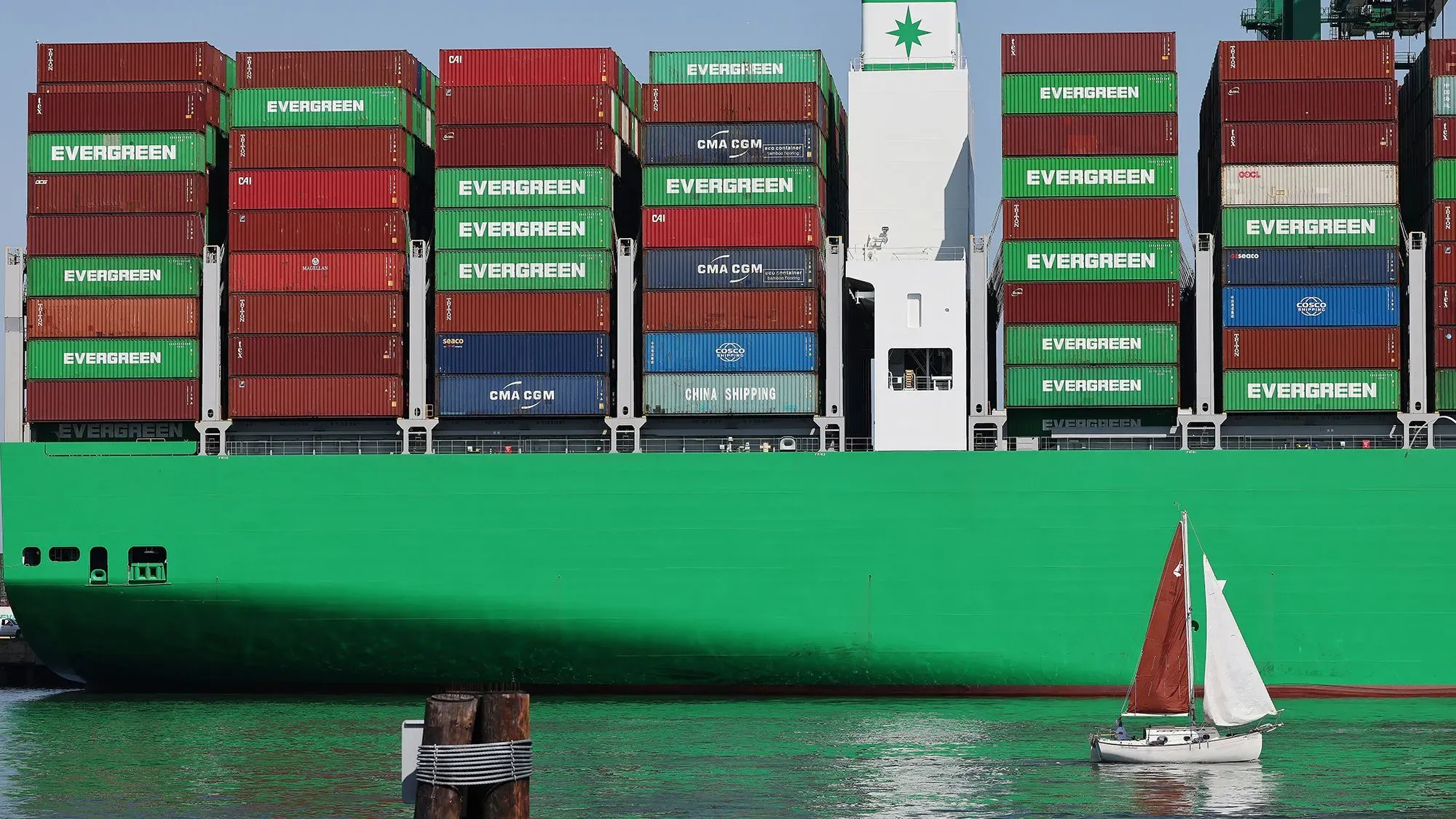 سفينة شحن كبيرة محملة بالحاويات الملونة، تبحر بجوار قارب صغير، تعكس نشاط التجارة العالمية وتأثير التعريفات الجمركية.