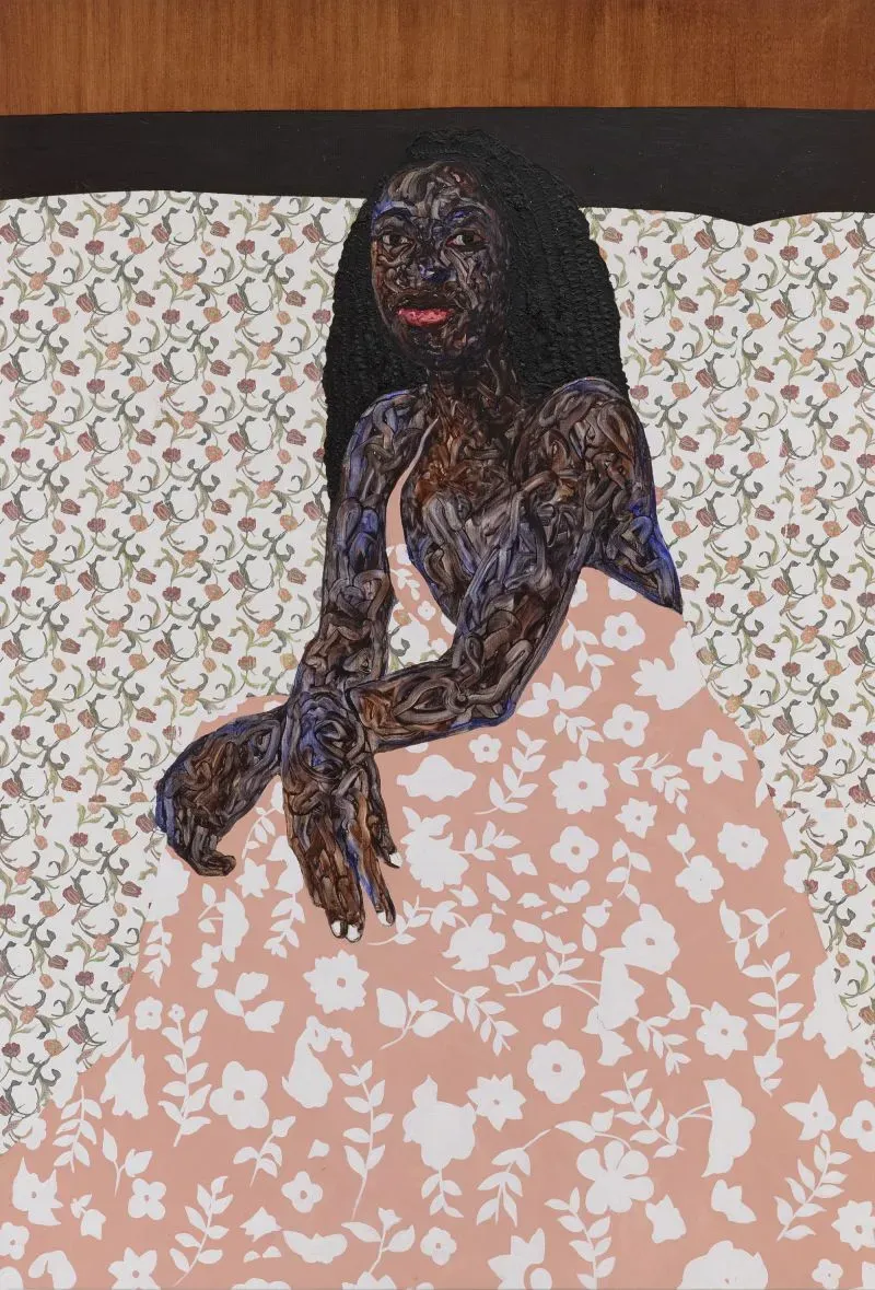 امرأة ذات بشرة داكنة تجلس على سرير مغطى بملاءة مزخرفة، ترتدي ثوبًا مزهرًا، مع تعبير وجه يعكس الثقة.