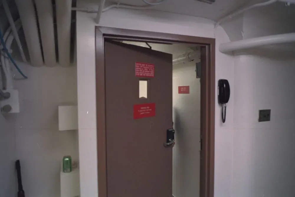 باب مدخل ملجأ سري تحت الأرض في البيت الأبيض، مع لافتات تحذيرية، يرمز إلى تاريخ البناء السري والتطورات الأمنية.