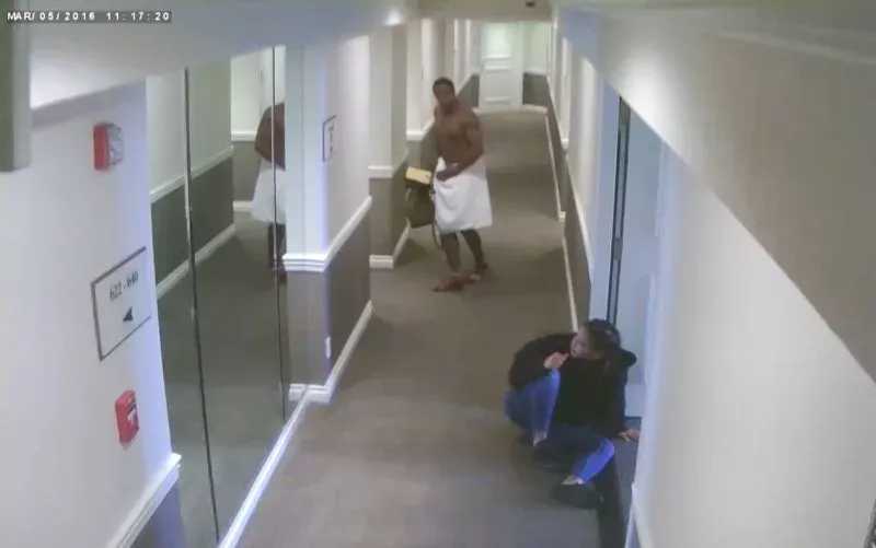 لقطة من فيديو مراقبة تُظهر شون 'ديدي' كومبس يتجول في ممر فندق، بينما تجلس امرأة على الأرض في حالة من القلق.