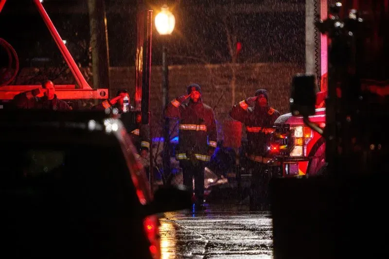 رجال الإطفاء في ملابسهم الرسمية يحيون تحية في أجواء ممطرة، أثناء جهود البحث عن ضحايا حادثة الطائرة في نهر بوتوماك.