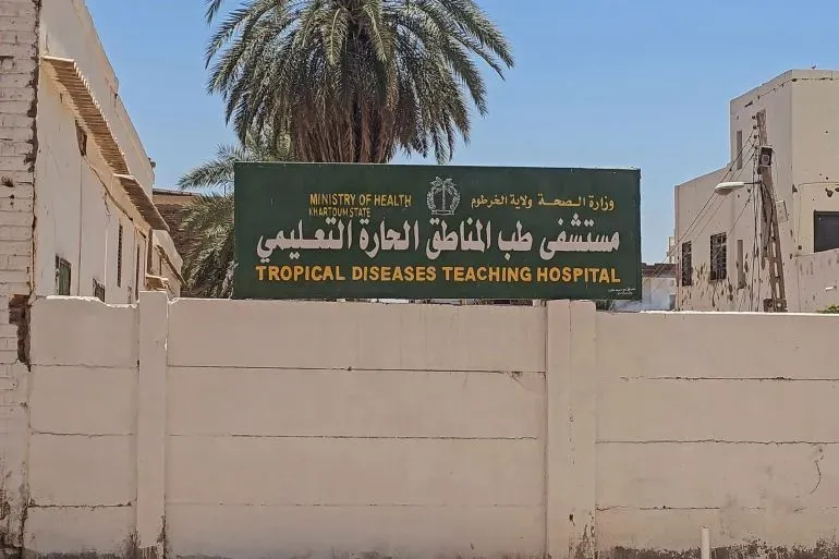 مستشفى الأمراض المدارية التعليمي في أمدرمان، يبرز لافتة باللون الأخضر تشير إلى خدماته الصحية وسط تحديات الحرب وانهيار النظام الصحي في السودان.