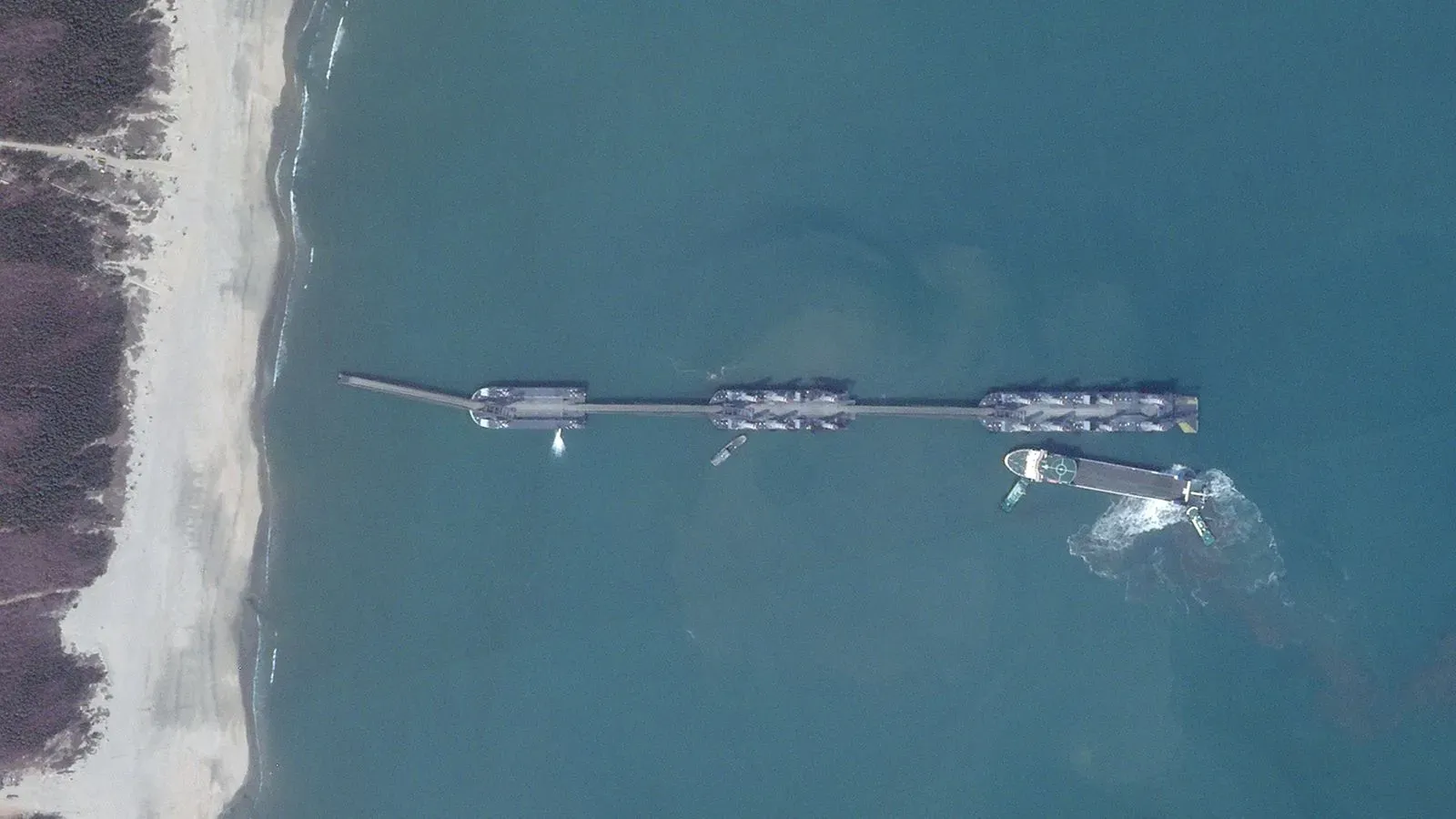 سفن ضخمة متمركزة قبالة شاطئ رملي في قوانغدونغ، تشكل جسراً يمتد أكثر من 800 متر، تعكس الابتكارات العسكرية البحرية الصينية.